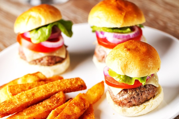 Mini hamburgers with tomato salad and cheese on wooden board