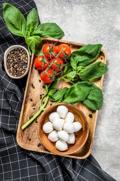 Mini mozzarella cheese, Basil leaves and cherry tomatoes, cooking Caprese salad. gray background. top view