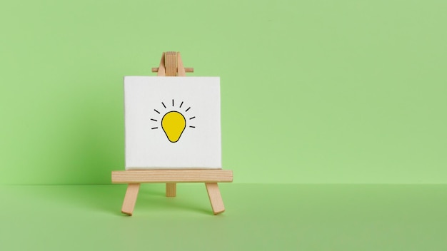 Mini painting on an easel on a green background With a painted light bulb Symbol of the mind ideas insight