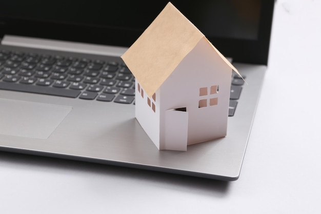 Mini paper house figurine and laptop on gray background