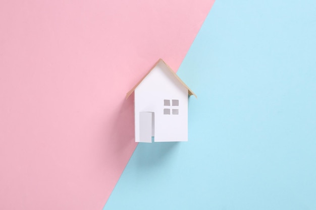 Mini paper house figurine on pink blue background Flat lay