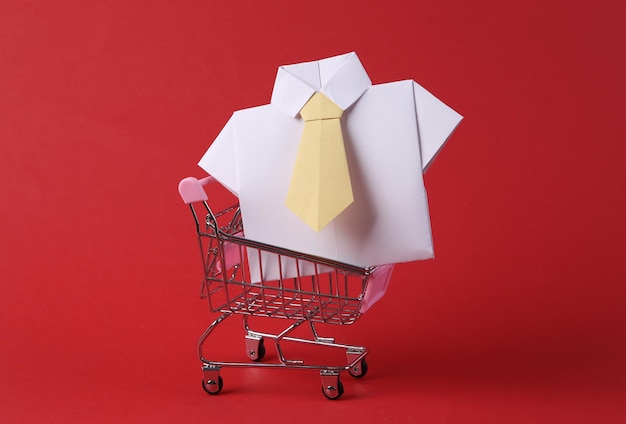 Mini shopping cart with origami shirt on red background