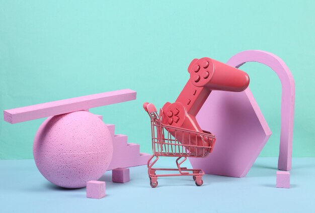 Mini shopping trolley with gamepad and pink geometric shapas on blue background Concept art Minimalism Creative layout