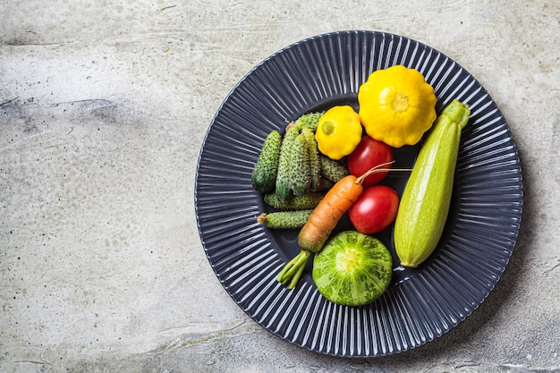 Mini vegetables concept. Mini zucchini, tomatoes, cucumbers, squash, and carrots on a dark plate.