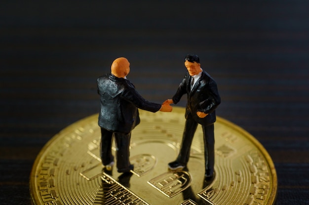 Miniature businessman handshake success deal business on Gold bitcoin.