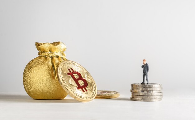 miniature businessman standing on the coins and looking to golden bitcoin