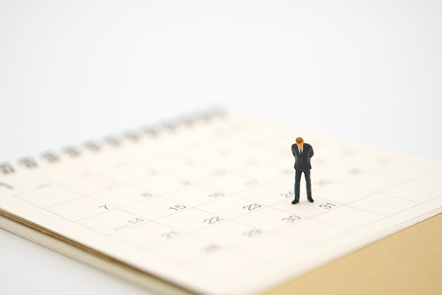 Miniature businessman standing on white calendar