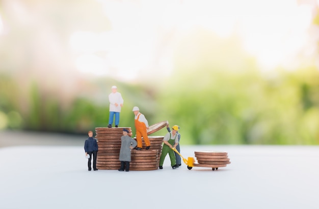 Miniature businessman and worker standing on the coins and carrying coins