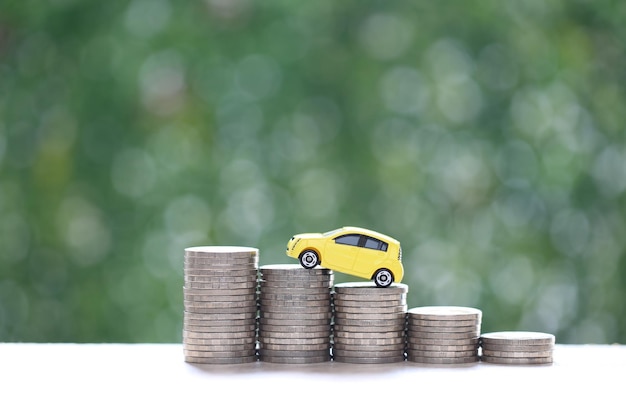 Miniature car model on growing stack of coins money on nature green background