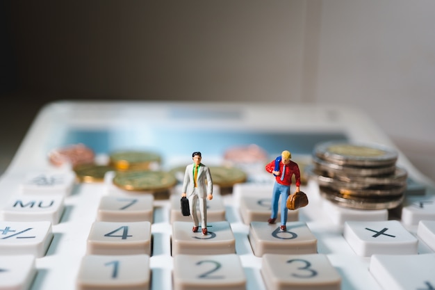 Miniature couple businessman standing on calculator with stack coins using as business and financial concept