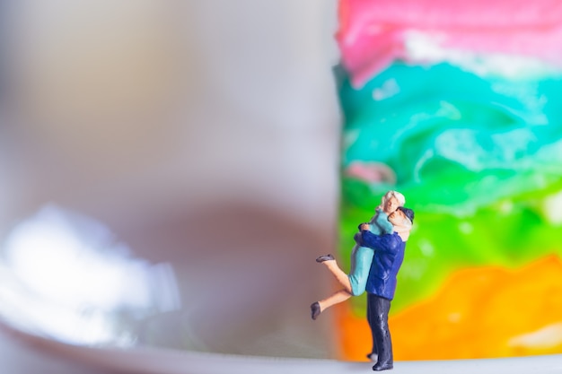 Miniature couple hugging in front of colorful background.