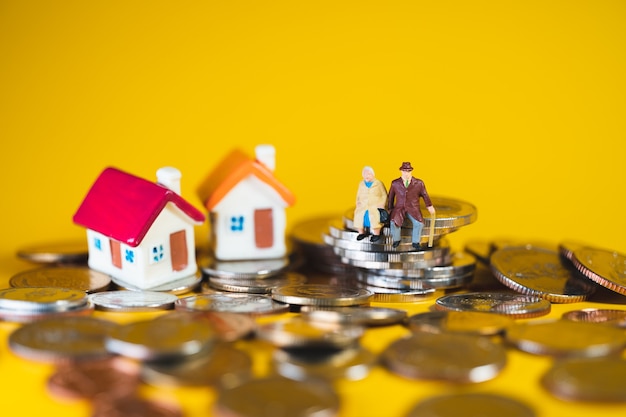 Miniature elderly people sitting on stack coins and mini house using as job retirement, business and insurance concept