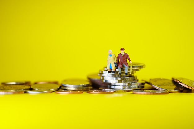 Miniature elderly people sitting on stack coins using as job retirement, business and insurance concept