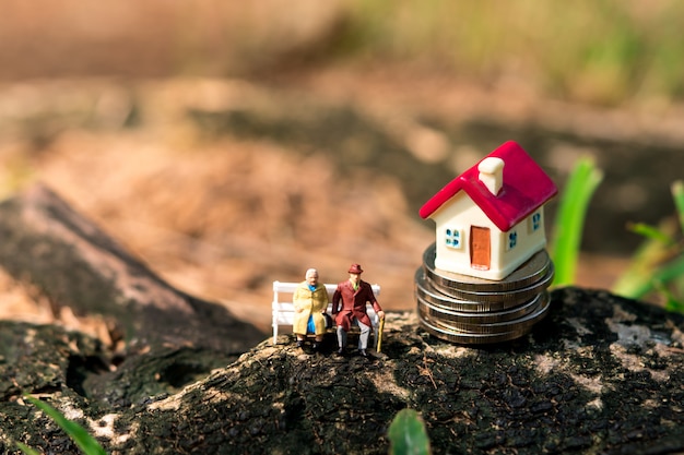 Miniature elderly people sitting with mini house on stack coins using as job retirement and family concept