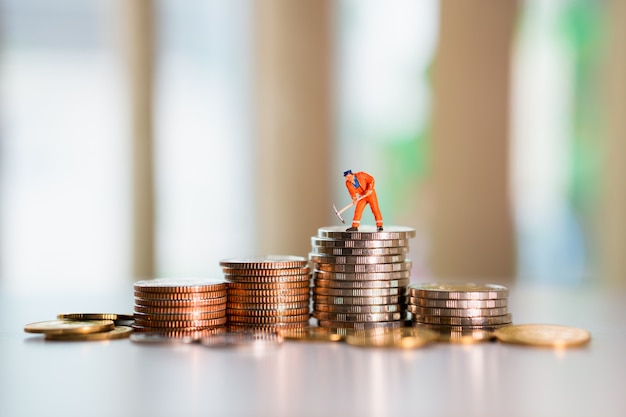 Miniature engineer wearing an orange suit on stack coins