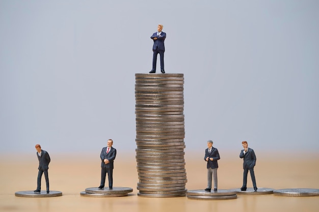 Miniature figure of five businessmen standing to different high and low coins stacking for position and successful business investment income concept