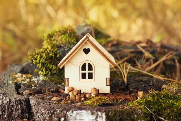 Photo a miniature figurine of a wooden house on a birch stump with moss and small mushrooms.