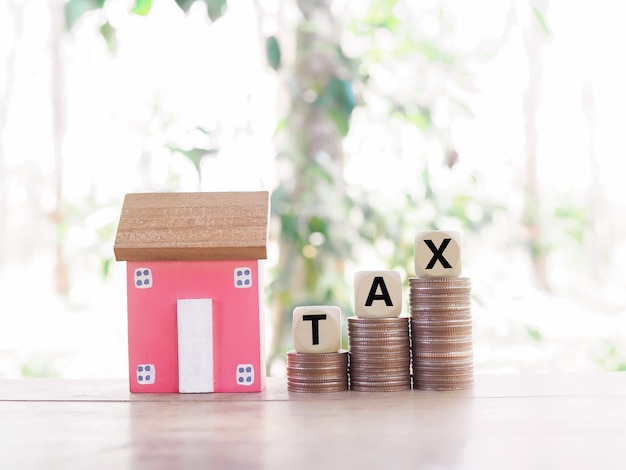 Miniature house and wooden blocks with the word TAX on stack of coins The concept of paying tax for house and property Property taxes