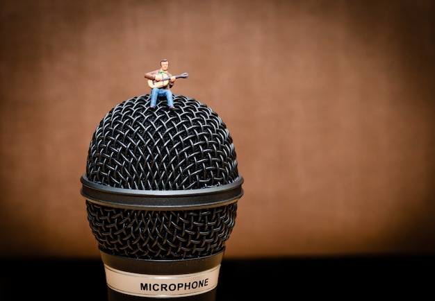 miniature man guitarist sitting on microphone and playing guitar