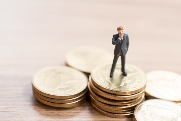 Miniature man standing on coins