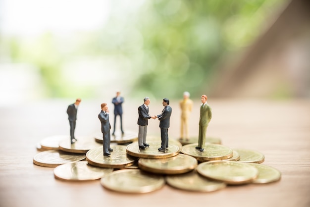 Miniature man standing on coins