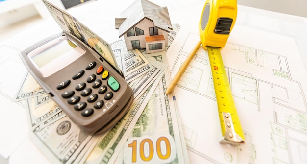 Miniature model of house against the background of a house plan, and money, and calculator.