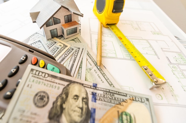 Miniature model of house against the background of a house plan, and money, and calculator.