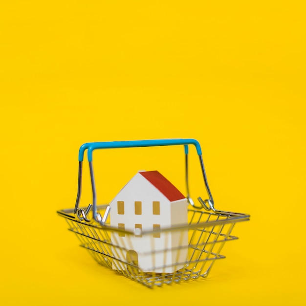 Miniature model of house in the shopping cart against yellow backdrop