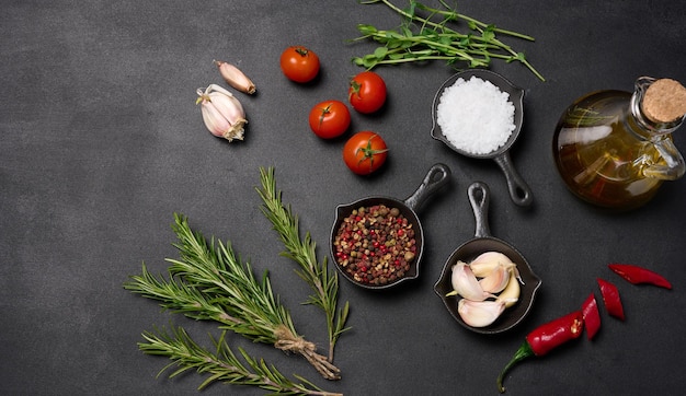 Miniature pans with spices salt black pepper and fragrant pepper a sprig of rosemary on a black table Spices for cooking