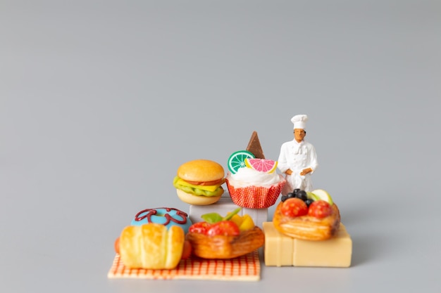 Miniature people Baker standing with Sweet dessert on grey background