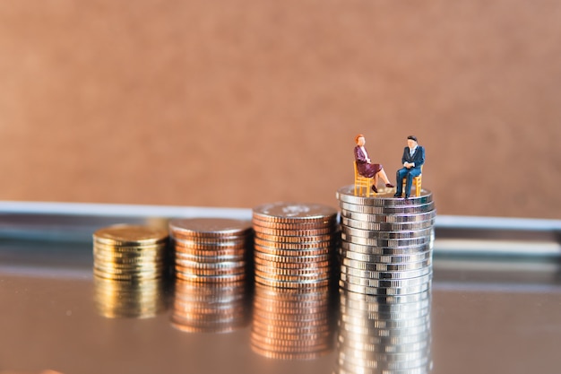 Miniature people, businessman and businesswoman sitting on stack coins using as business teamwork and financial concept