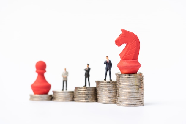 Miniature people, businessmen standing on stack of coins with red chess piece. 