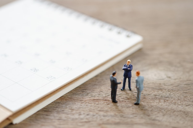 Miniature people businessmen standing on white calendar using as background business concept