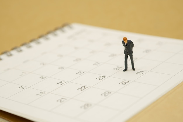 Miniature people businessmen standing on white calendar