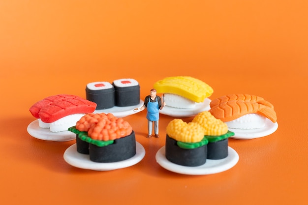 Miniature people ,Chef making Sushi set on orange background