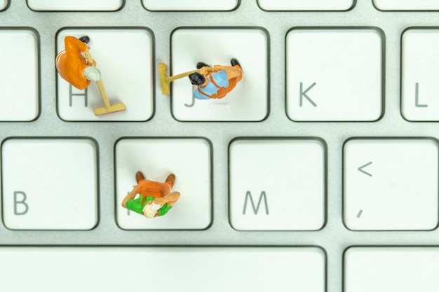 Miniature people cleaning white keyboard computer.