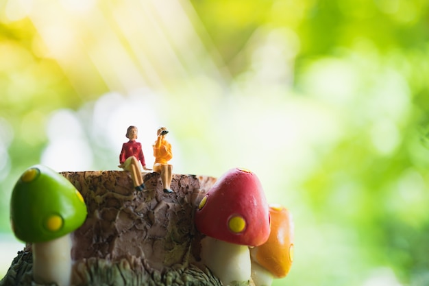 Miniature people, couple woman sitting on mushroom timber, woman sitting on green nature background 