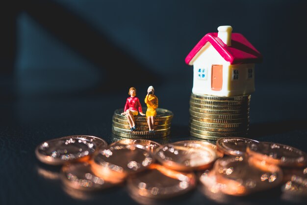 Miniature people, couple woman sitting on stack coins and mini house using as business and property 