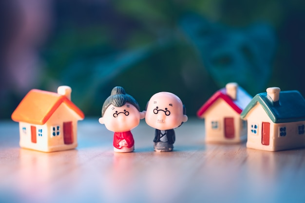 Miniature people, elderly man and woman standing with mini house using as job retirement and insurance concept