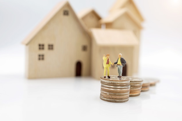 Miniature people: Elderly person standing on coins stack with home, Retirement planning concept.