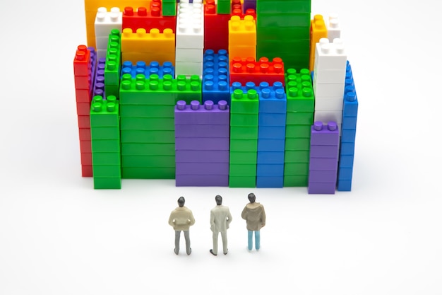 Miniature people figures of people stand near the colored blocks of a plastic constructor on a white background in the form of multistorey buildings concept of modern buildings and houses