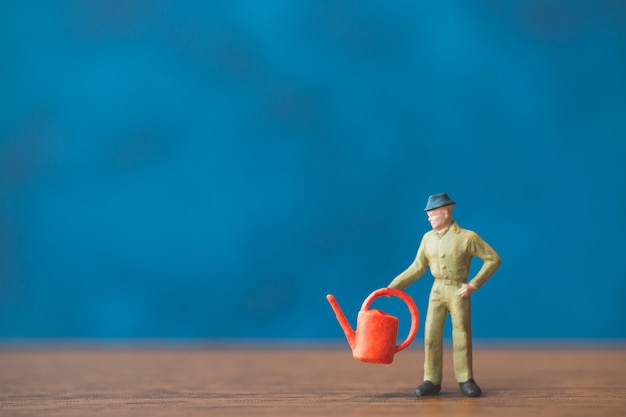 Miniature people gardener standing in front of a blue wall background