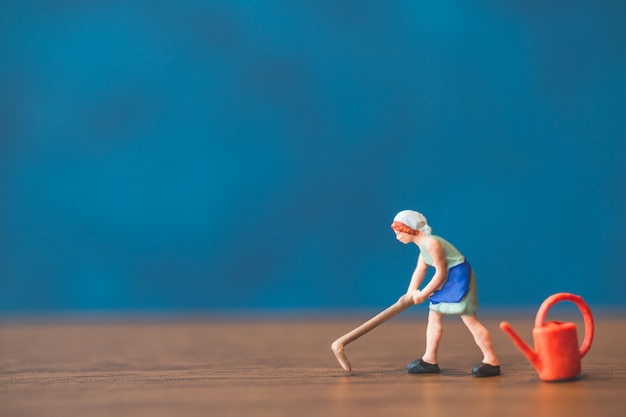 Miniature people gardener standing in front of a blue wall background