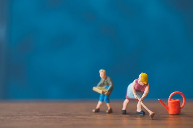 Miniature people gardener standing in front of a blue wall background