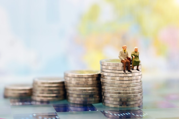 Miniature people: Happy senior couple sitting on coins stack, Retirement Concept.