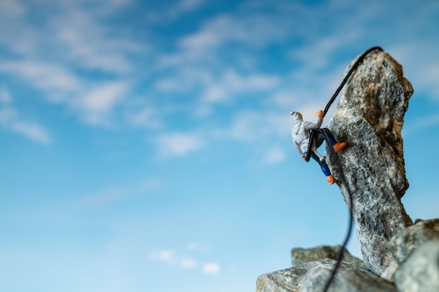 Photo miniature people: hikers climbing up on the rock . sport and leisure concept.