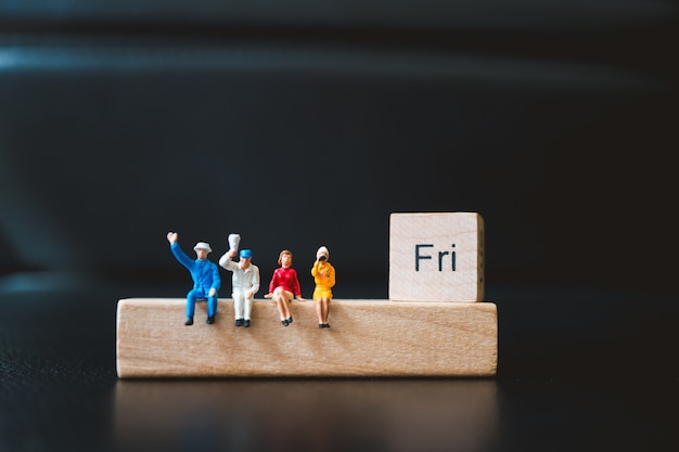 Miniature people, man and woman sitting with friday wooden block using as business concept