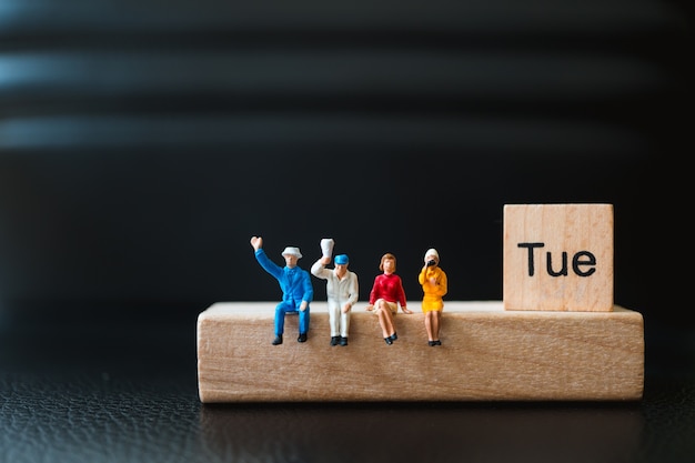 Miniature people, man and woman sitting with tuesday wooden block using as business concept