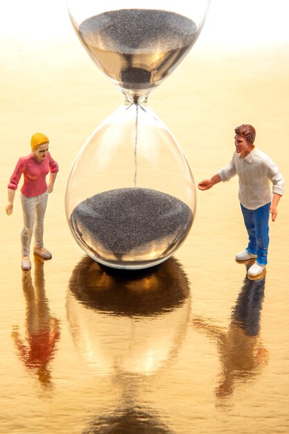 Photo miniature people man and woman stand near an hourglass against a white background concept of people life time in society