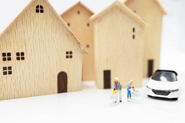 Miniature people: Parent and children with shopping cart standing on coins stack with house and car.  Concept of shopping in housing and vehicles.